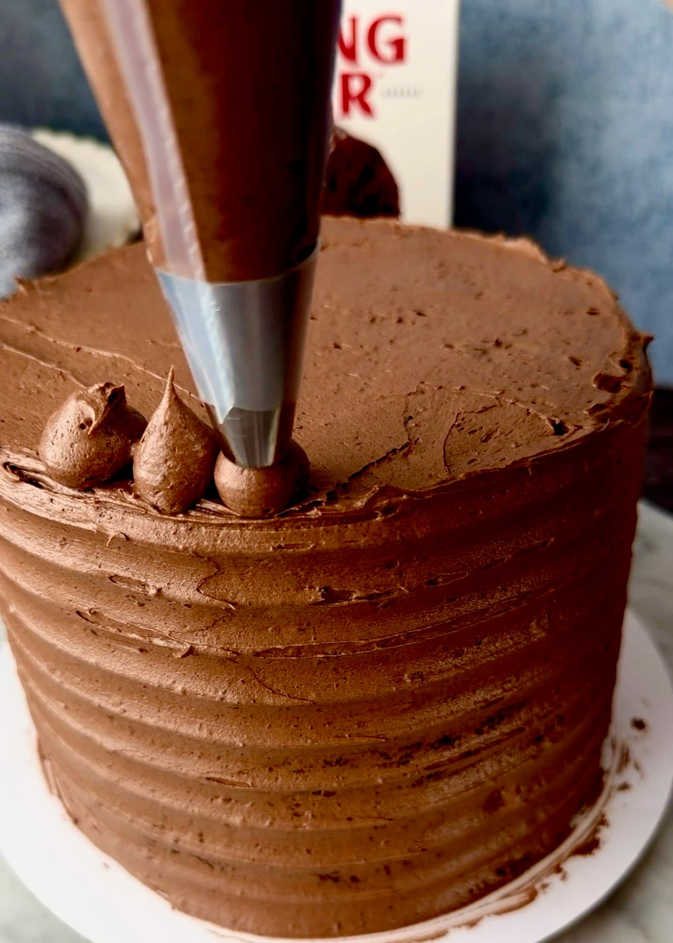 Chocolate buttercream being piped in neat dollops along a frosted cake