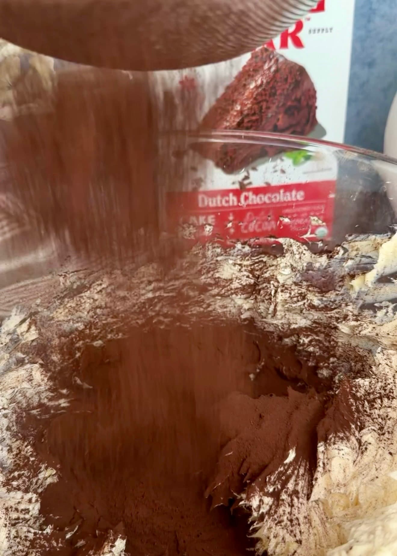 Cocoa powder falling through a sieve onto creamed butter in a glass bowl
