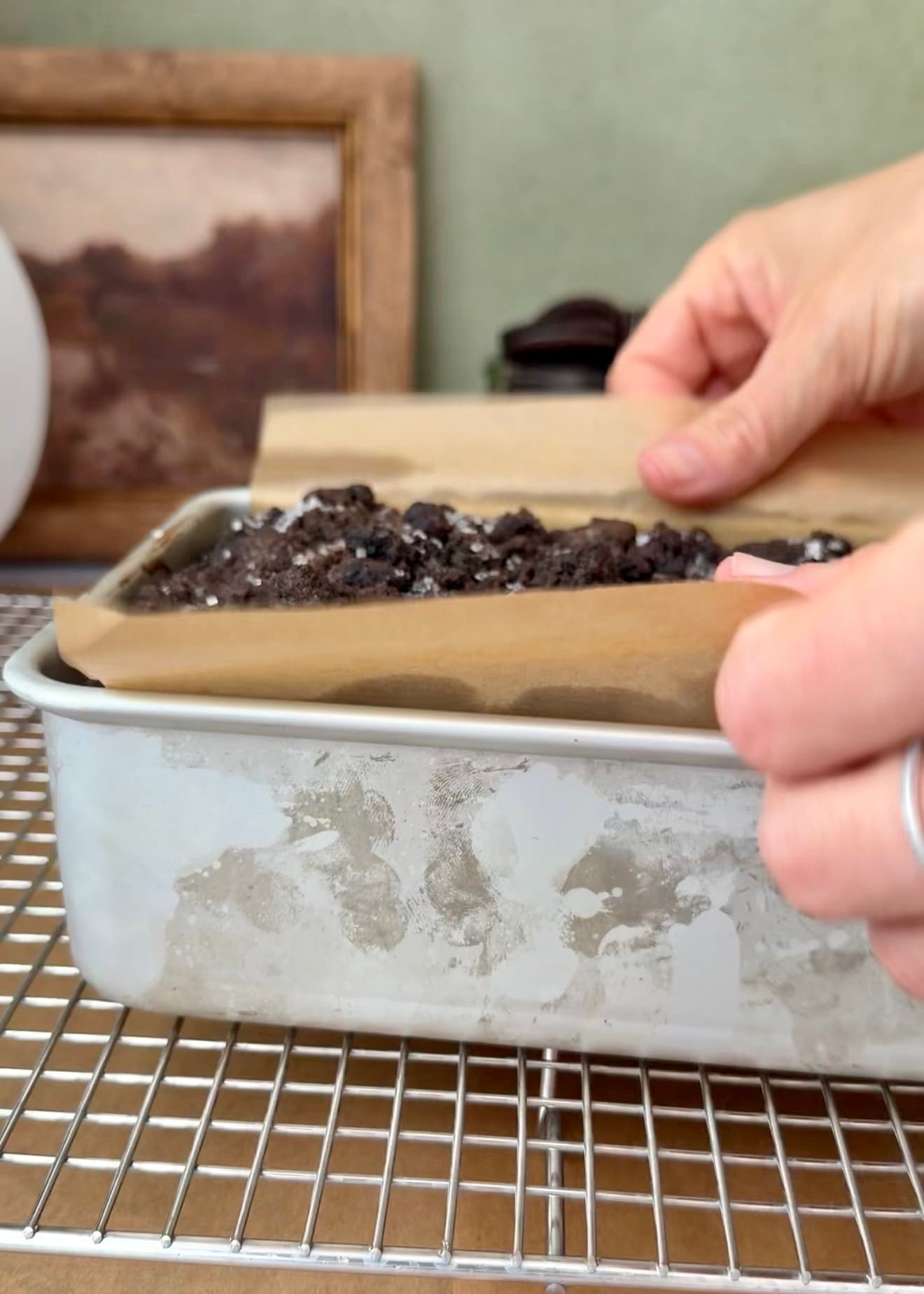 Hands lifting the parchment edges around the baked loaf