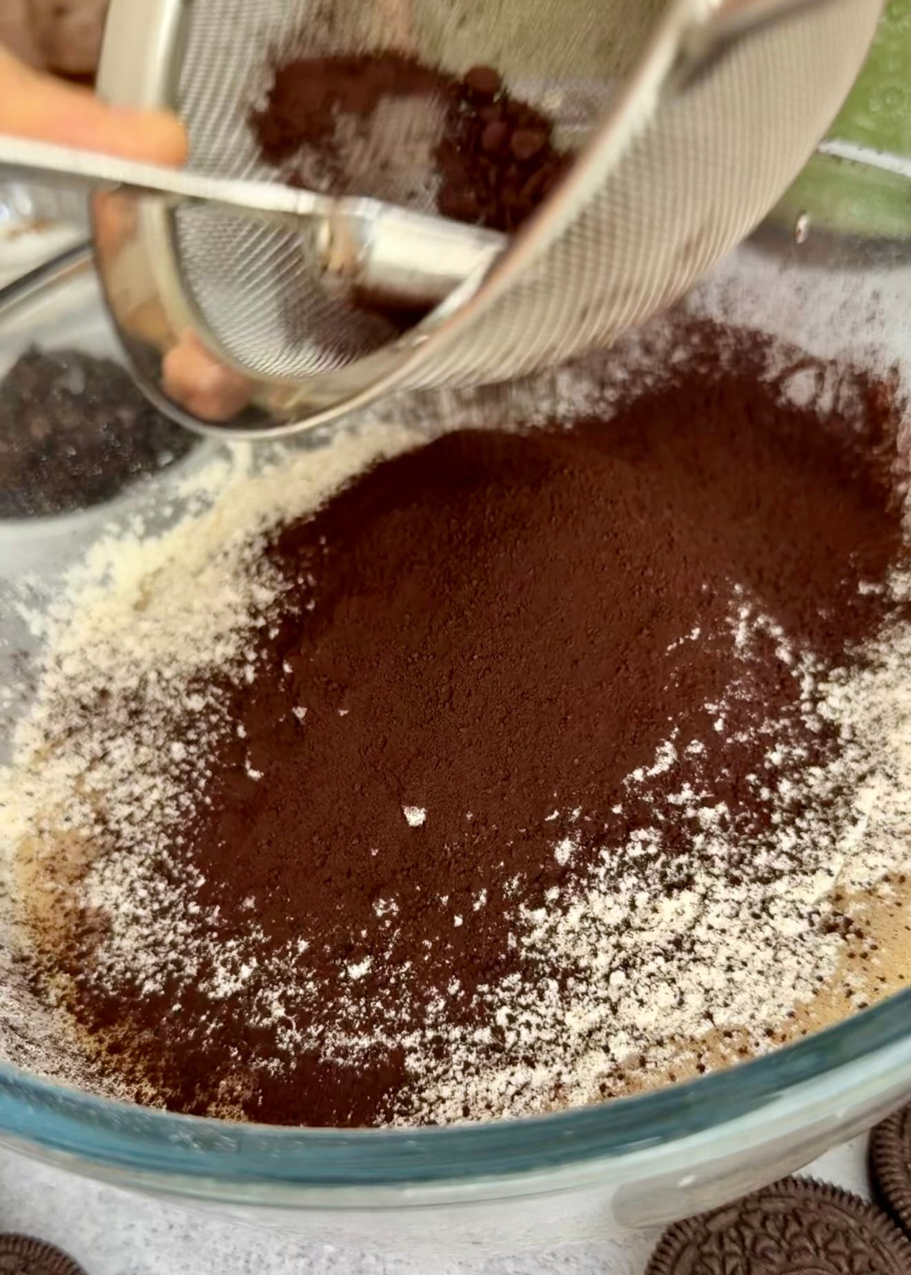 Cocoa passing through a sieve over the batter ingredients