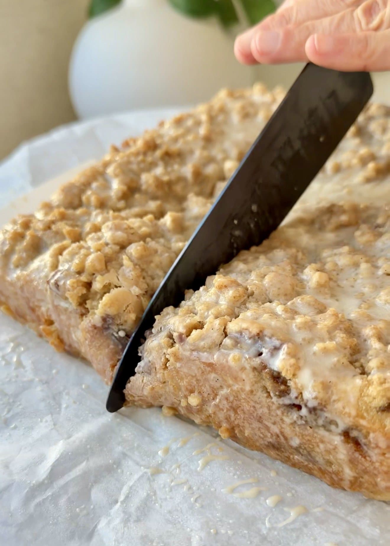 A knife slicing through the glazed cinnamon roll coffee cake