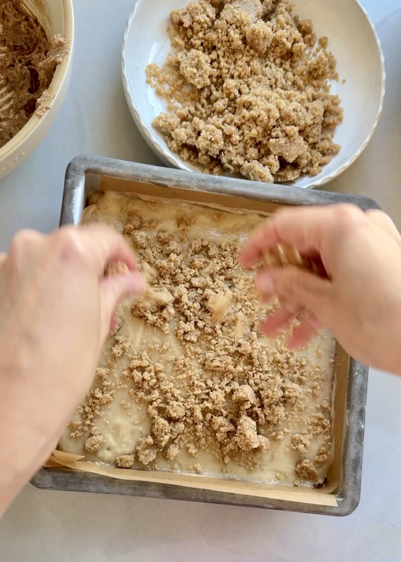 Buttery cinnamon streusel being scattered over the coffee cake batter