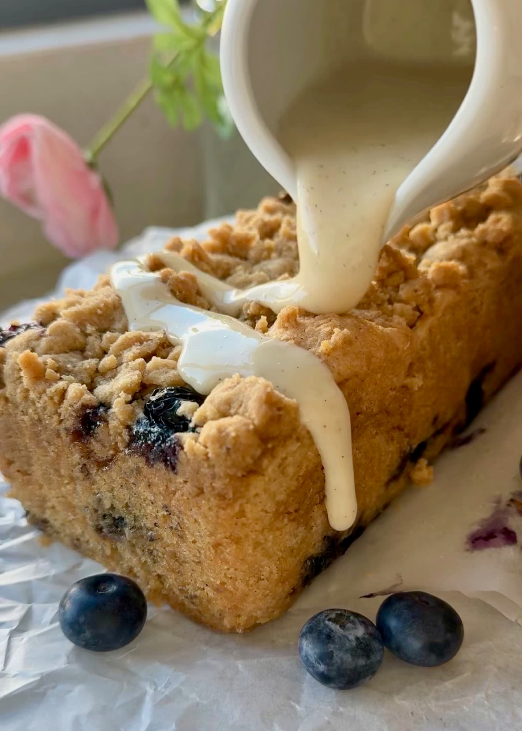 Vanilla bean glaze being poured over a baked Gluten-Free Blueberry Coffee Cake loaf
