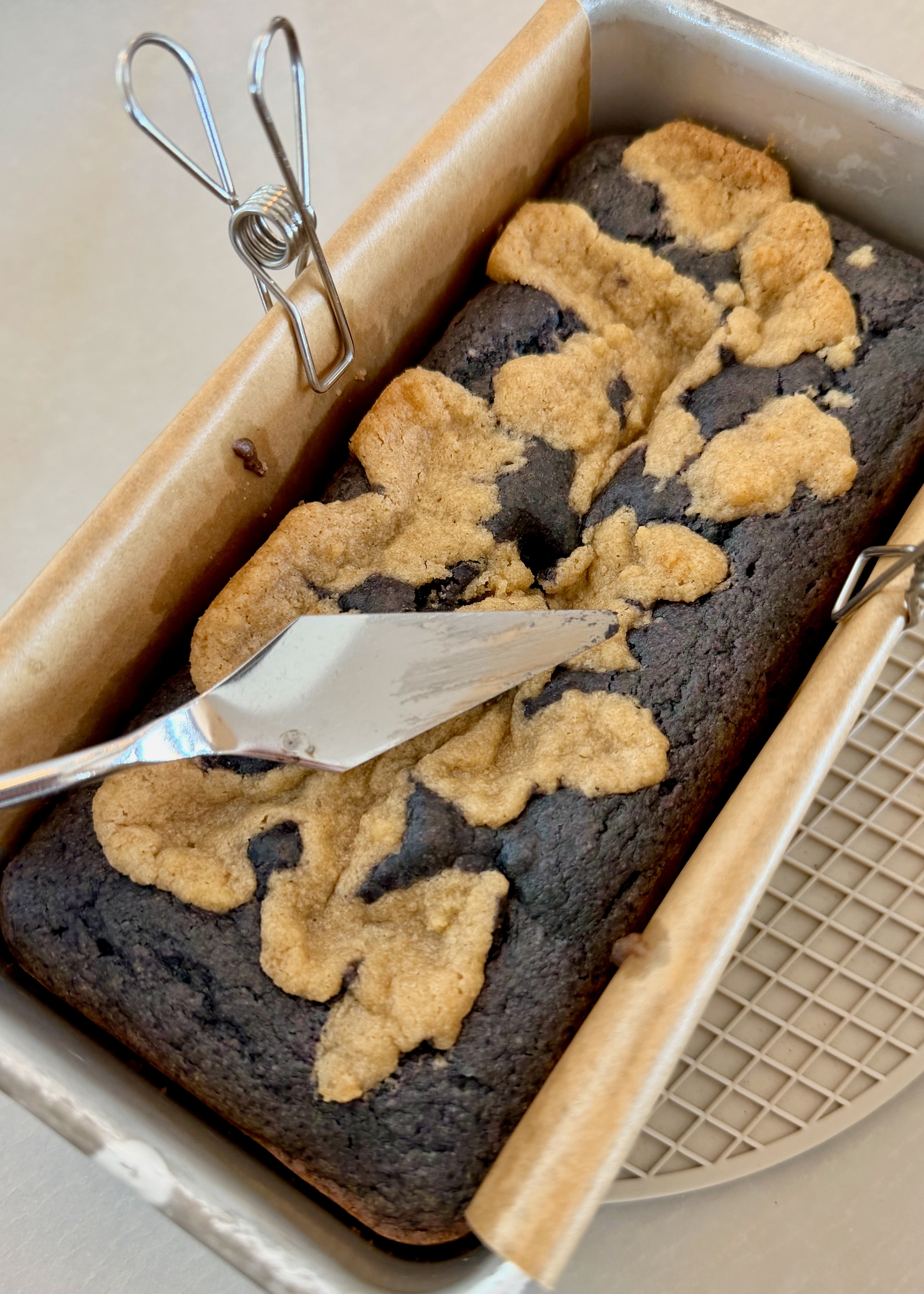 A knife with a thin coating of blueberry cake residue resting over the baked loaf
