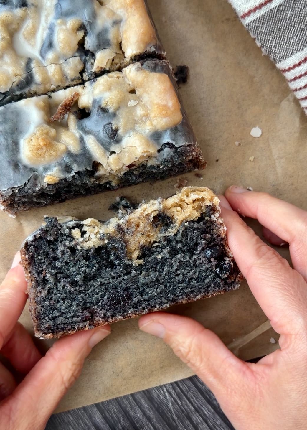A held slice showing purple blueberry crumb, crumble, and glaze