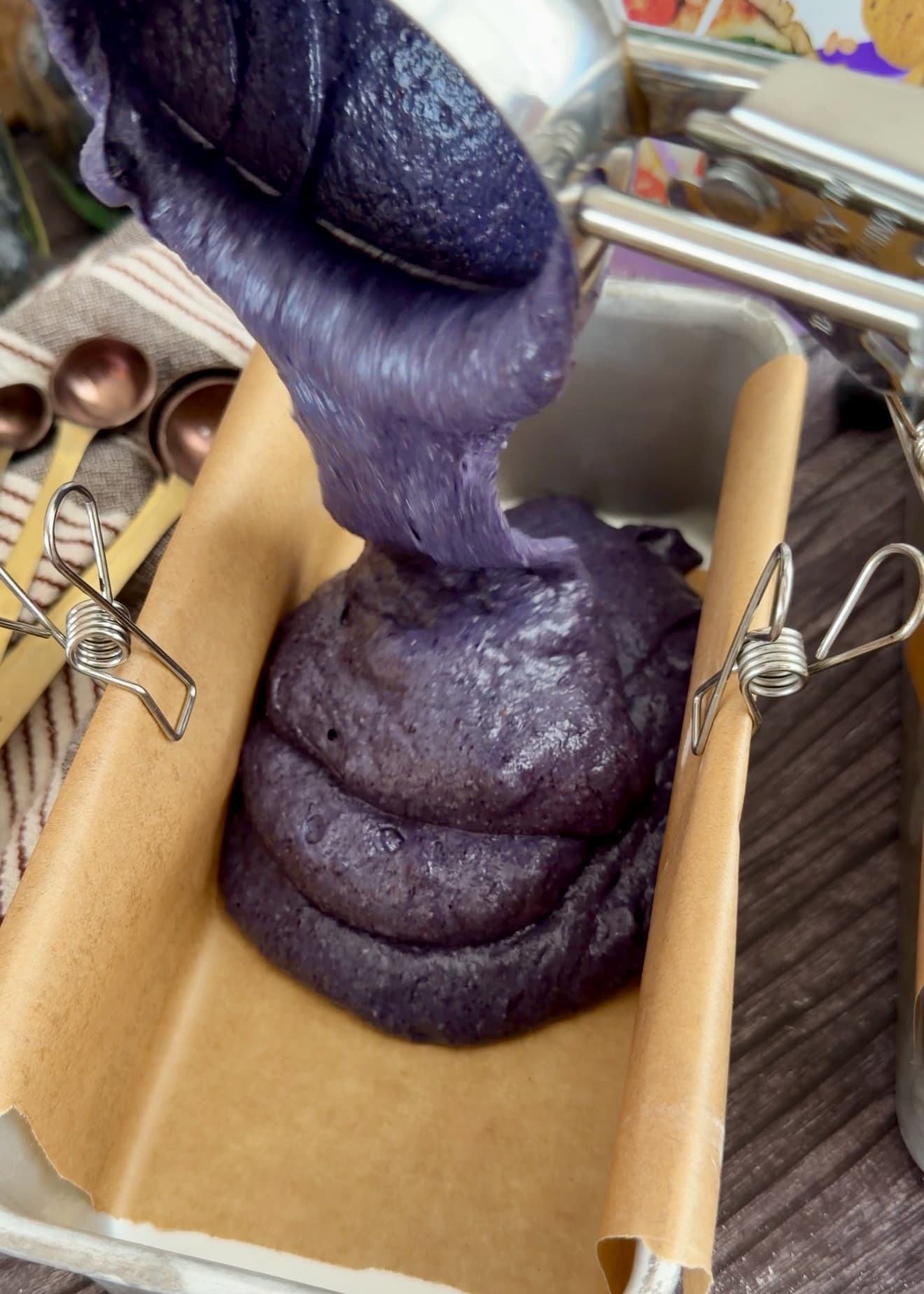 Purple blueberry batter being poured into a parchment-lined mini loaf pan