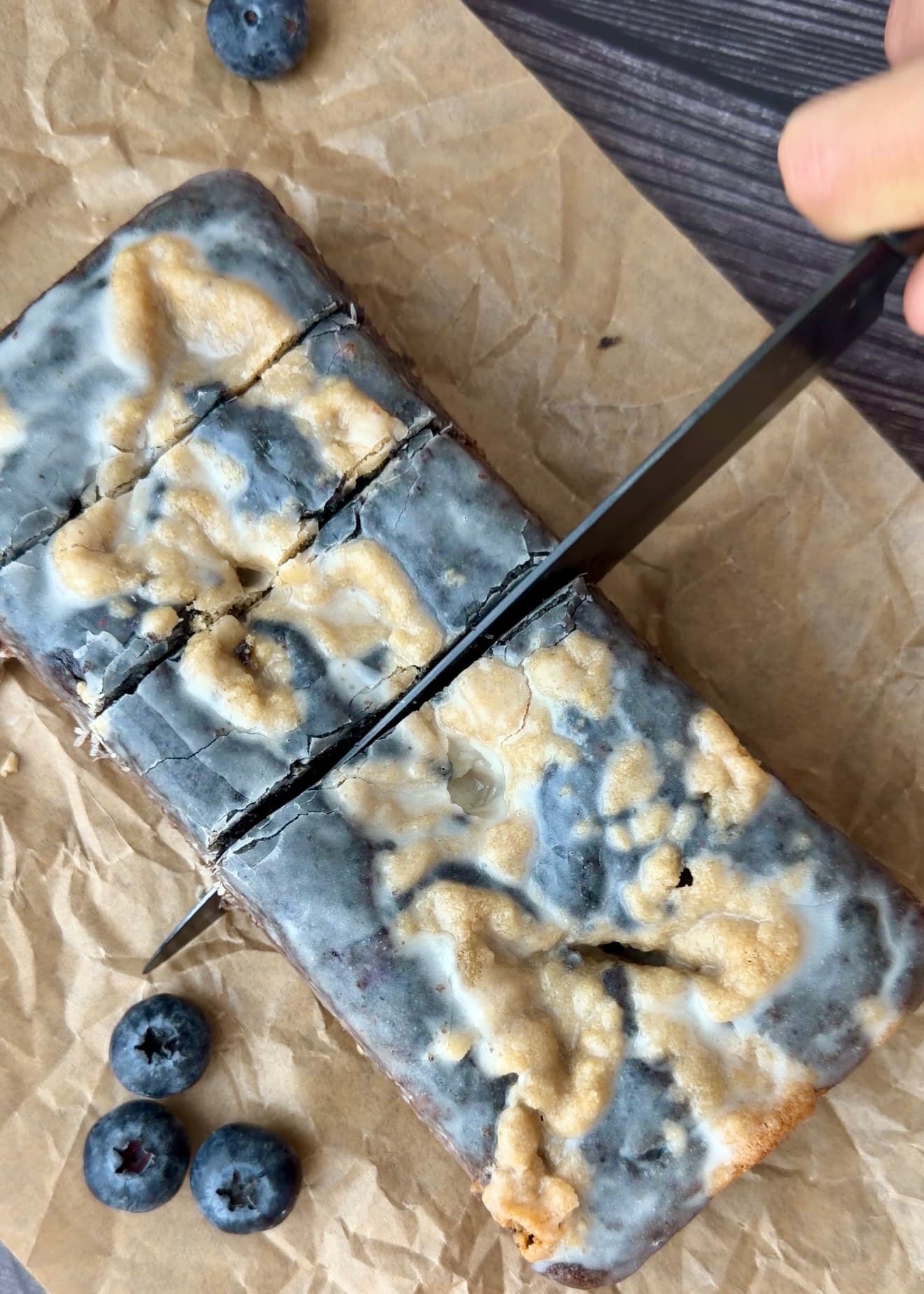 A knife slicing a glazed blueberry loaf on parchment