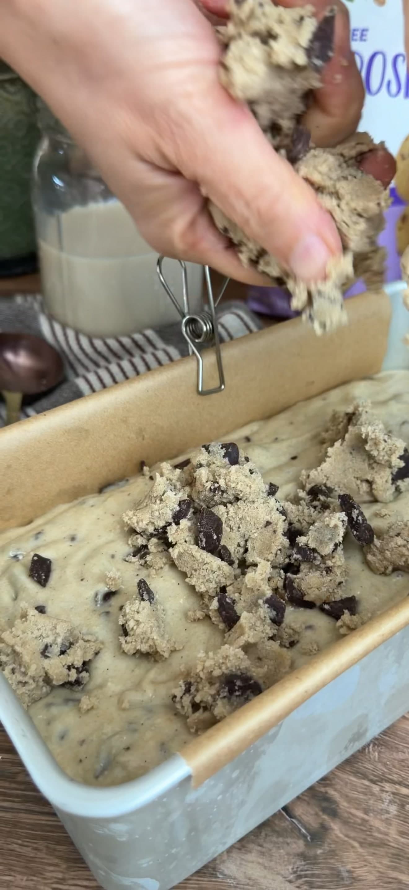 A hand breaking chocolate chip streusel over the loaf batter