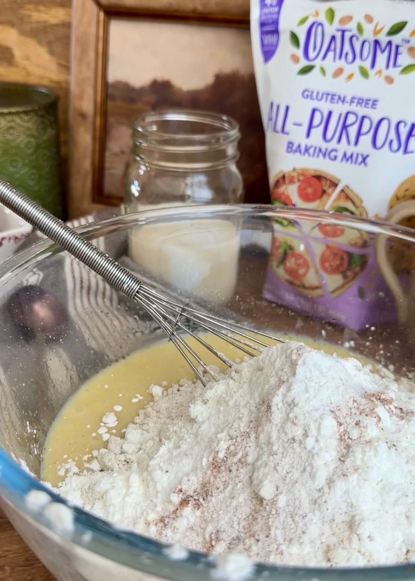 Dry ingredients piled over the wet mixture with a whisk in the bowl