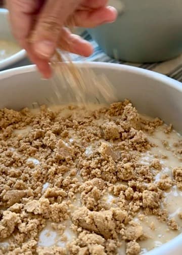 Cinnamon streusel being sprinkled over vanilla cake batter