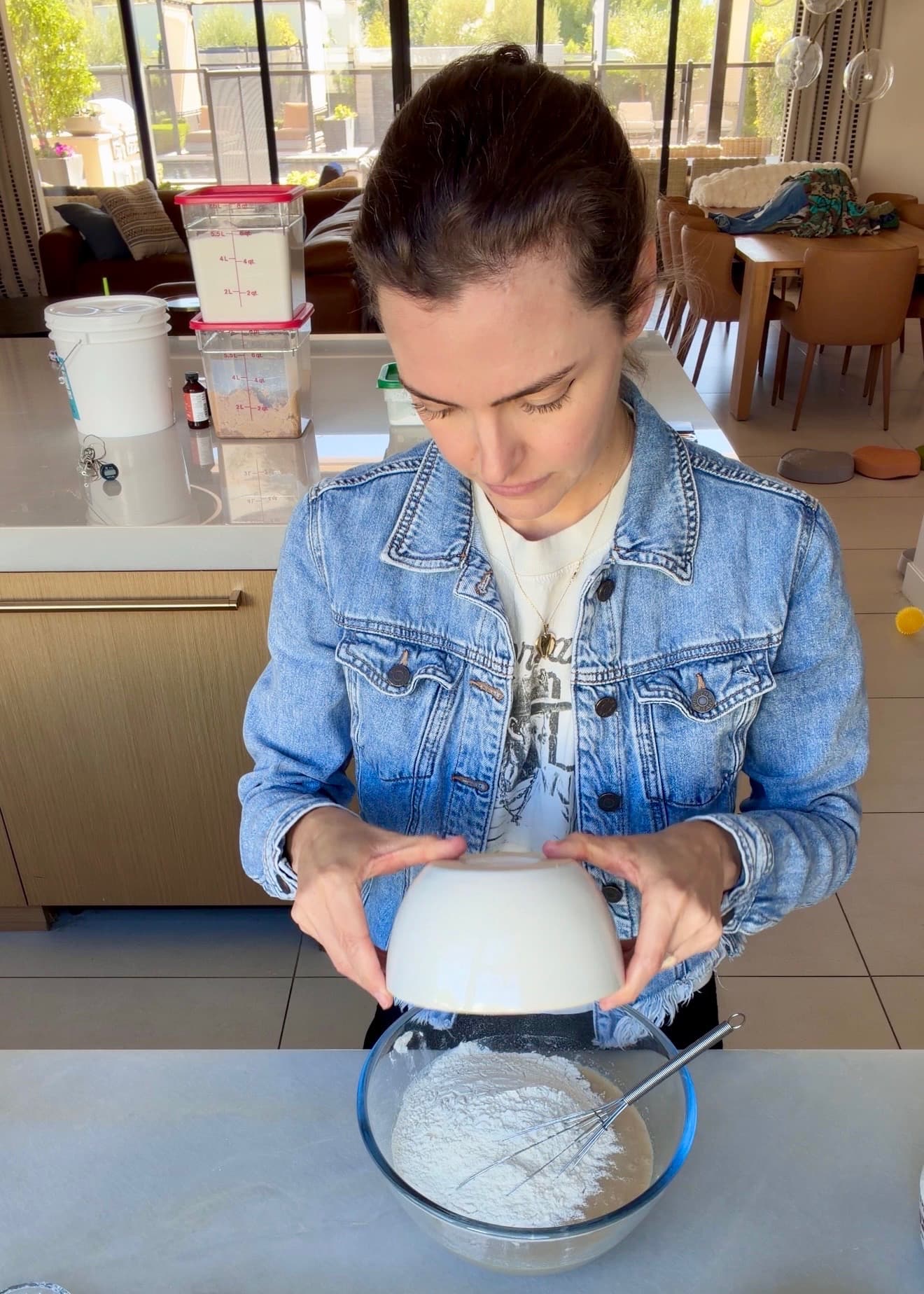 Flour being tipped over the wet cake ingredients with a whisk resting in the bowl