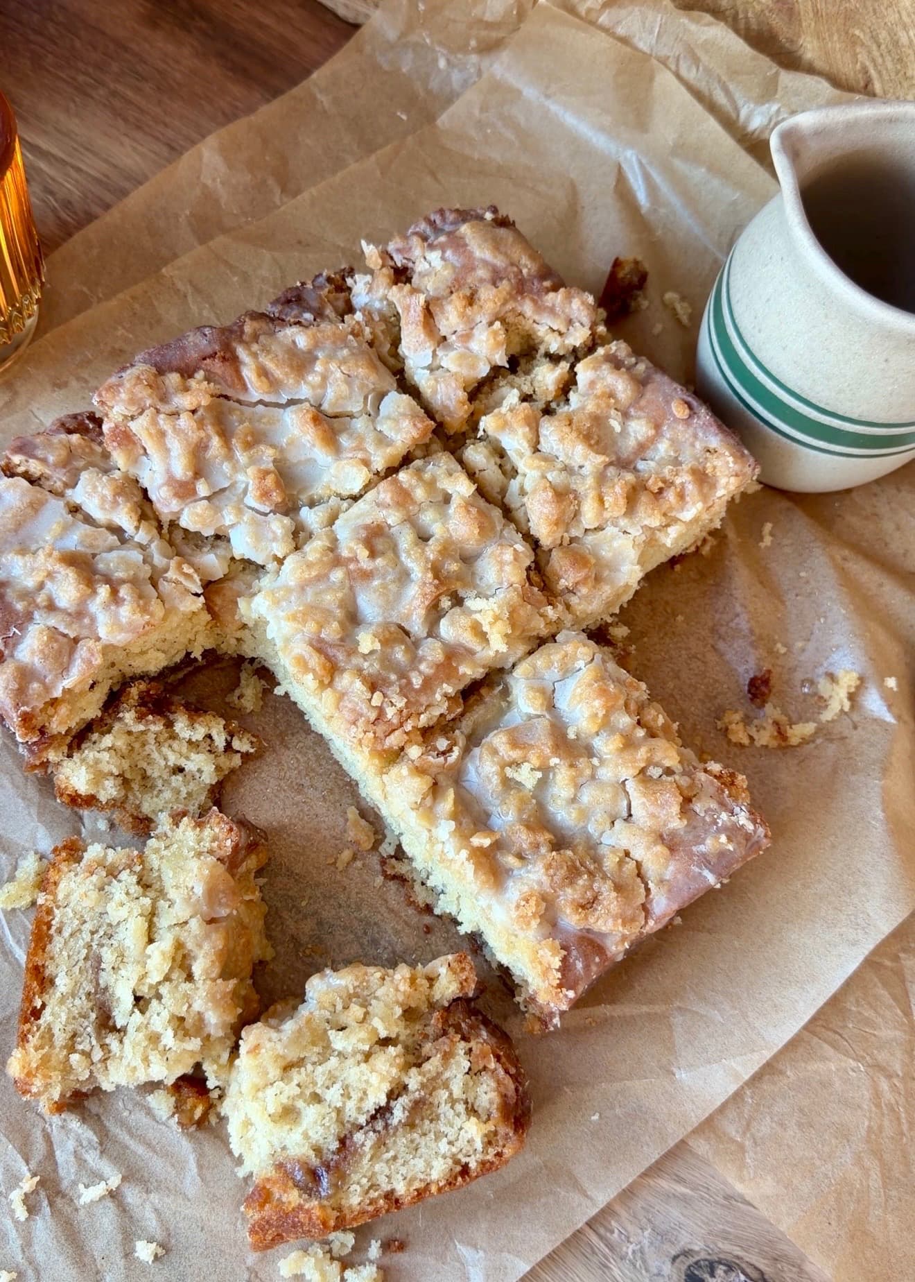 Cut squares of glazed Maple Fritter Coffee Cake on parchment beside a striped mug