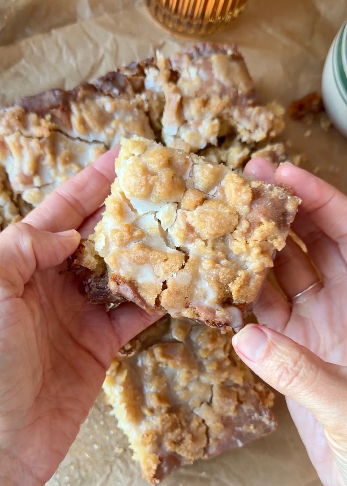 Hands holding a square of coffee cake beneath its glazed crumble topping