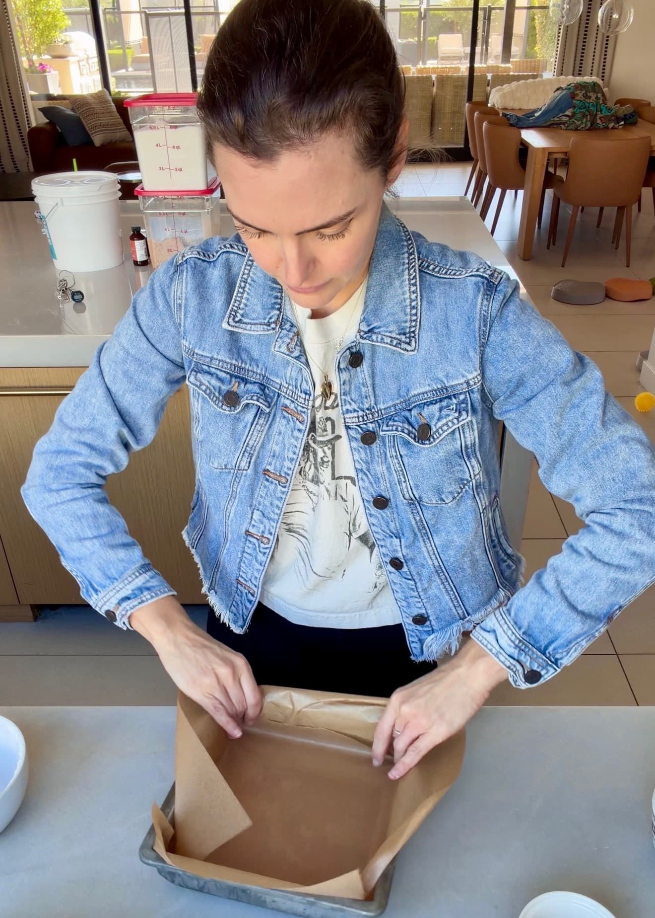 Hands pressing crossed sheets of parchment into a square baking pan