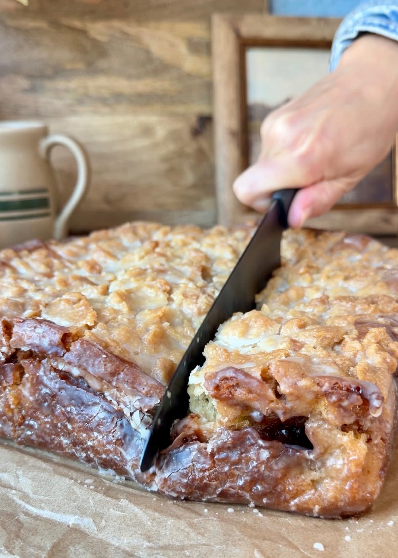 A knife cutting down through the glazed crumble and browned cake edge