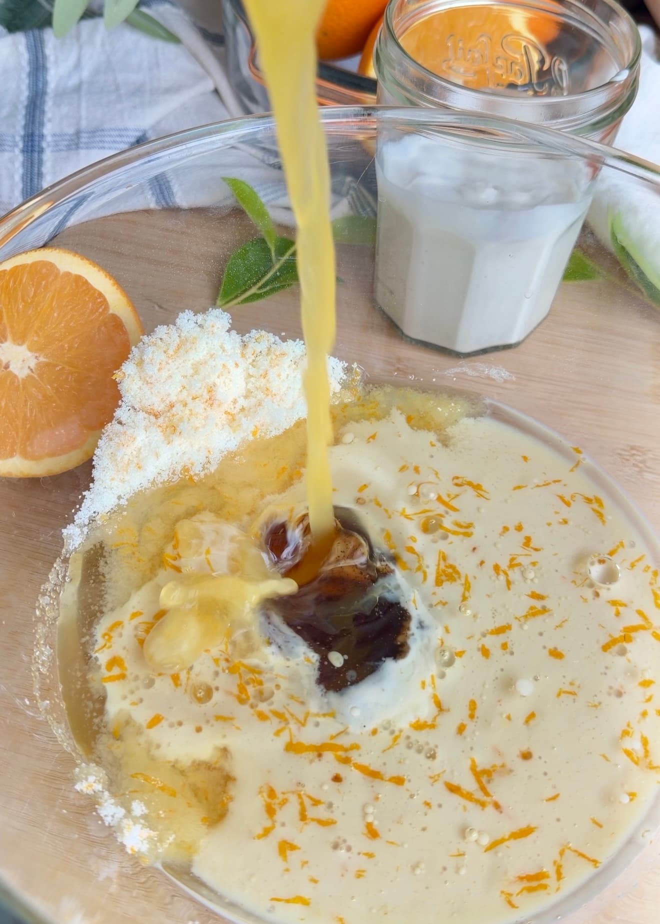 Orange-colored liquid being poured into a bowl of wet ingredients and zest