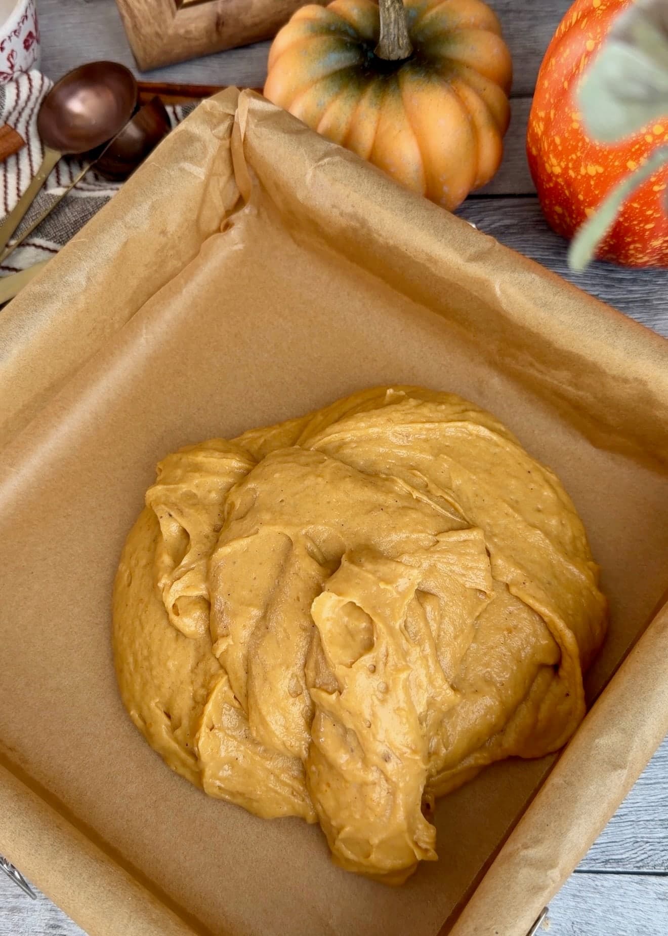 Pumpkin batter scooped into a square pan lined with overlapping parchment