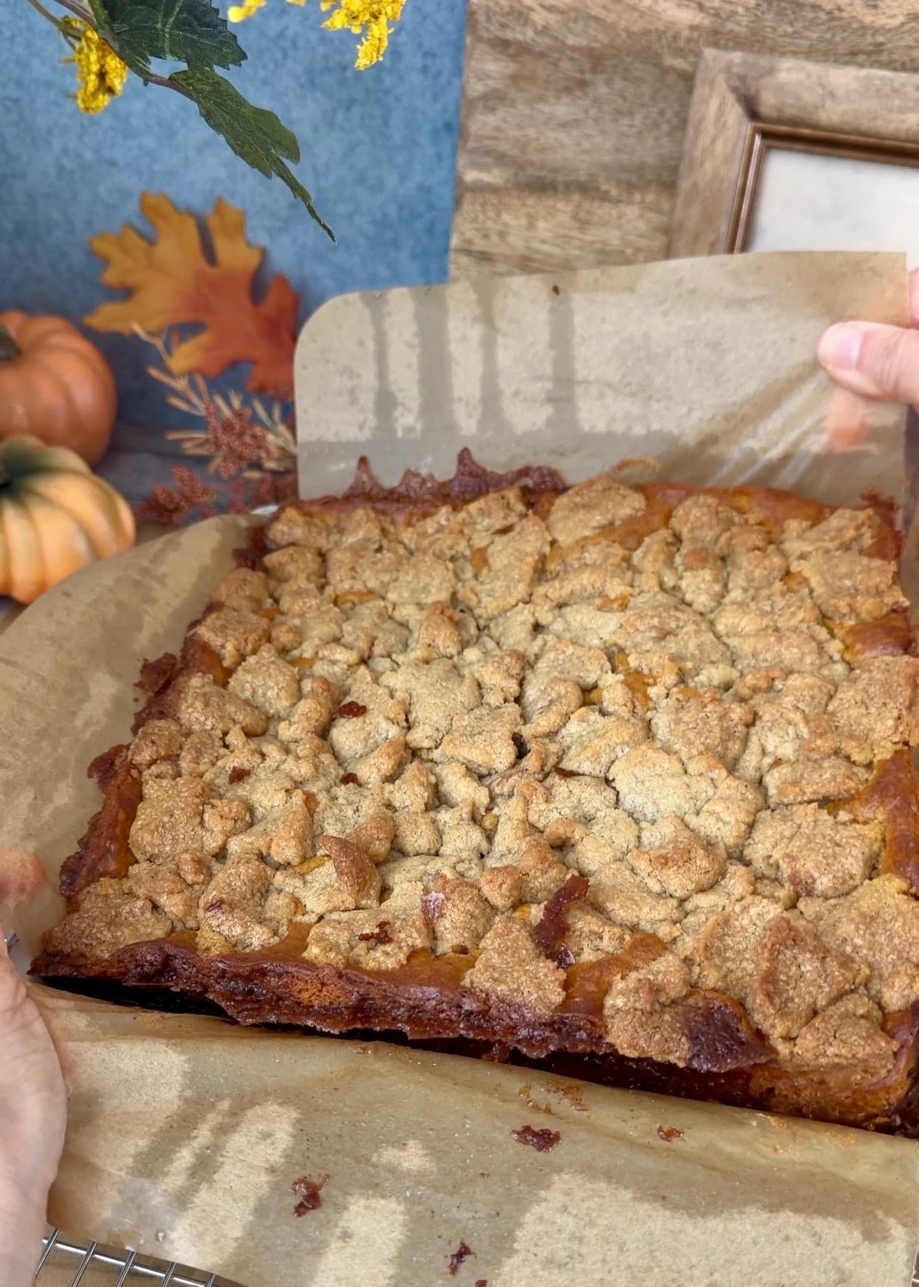 Hands peeling parchment away from the baked cake on a cooling rack