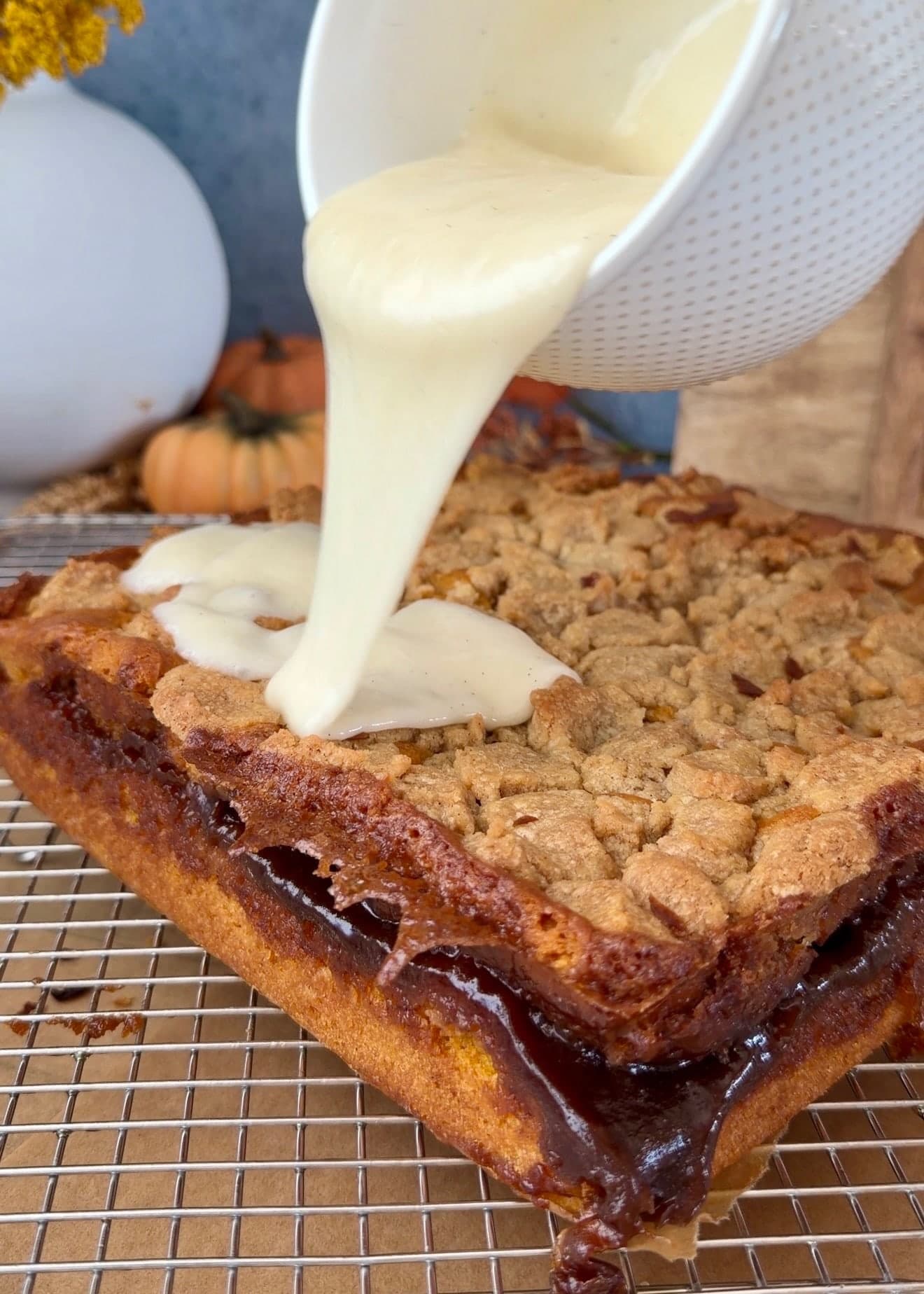 Vanilla glaze pouring from a bowl over the baked crumble topping