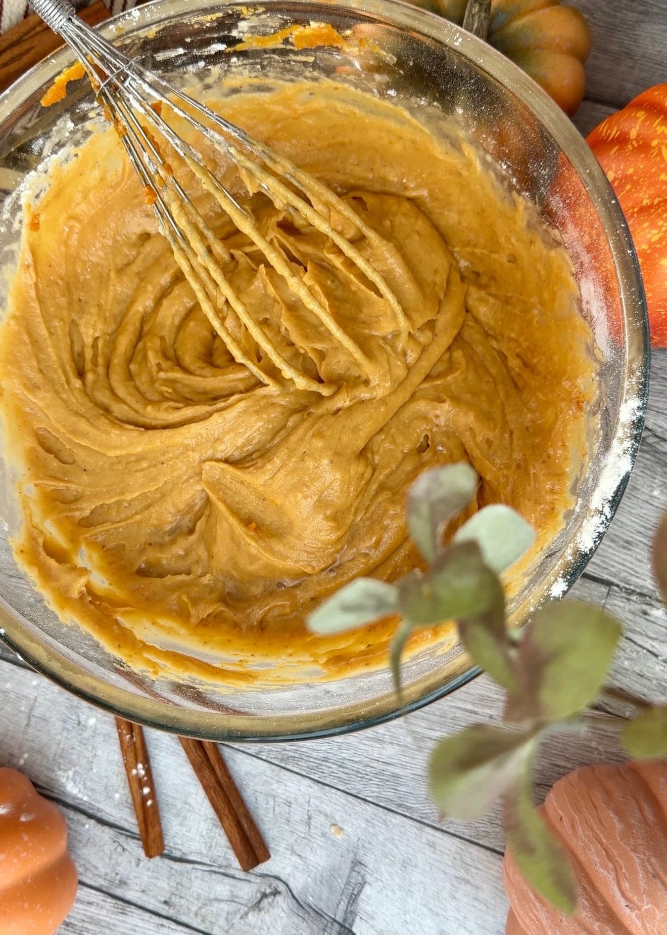 Thick orange pumpkin batter holding whisk trails in a glass bowl