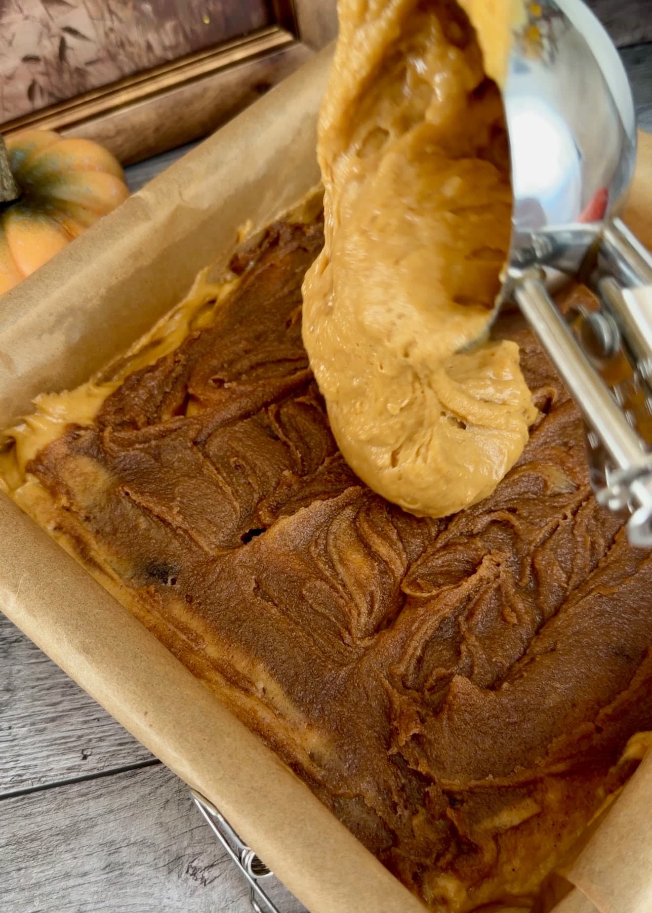 A scoop dropping pumpkin batter onto the cinnamon layer