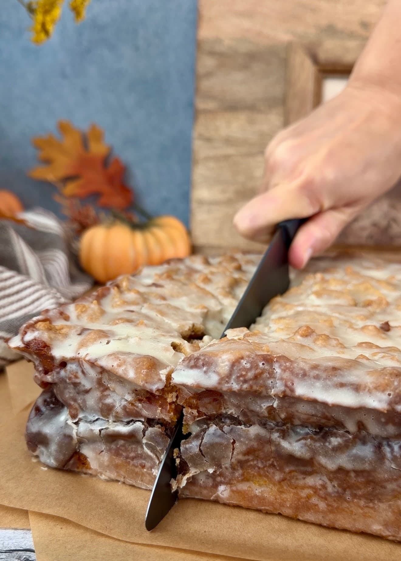 A serrated knife cutting through the glazed pumpkin coffee cake