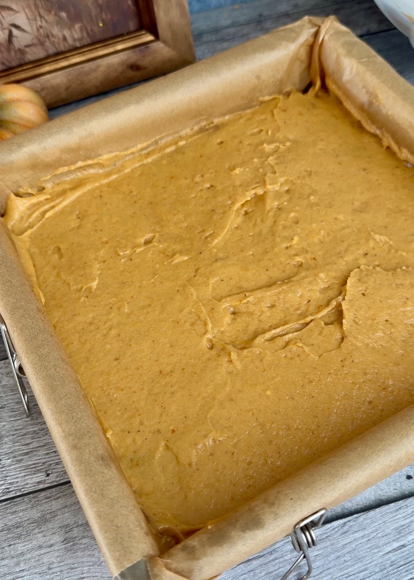 A smooth top layer of pumpkin batter filling a parchment-lined pan
