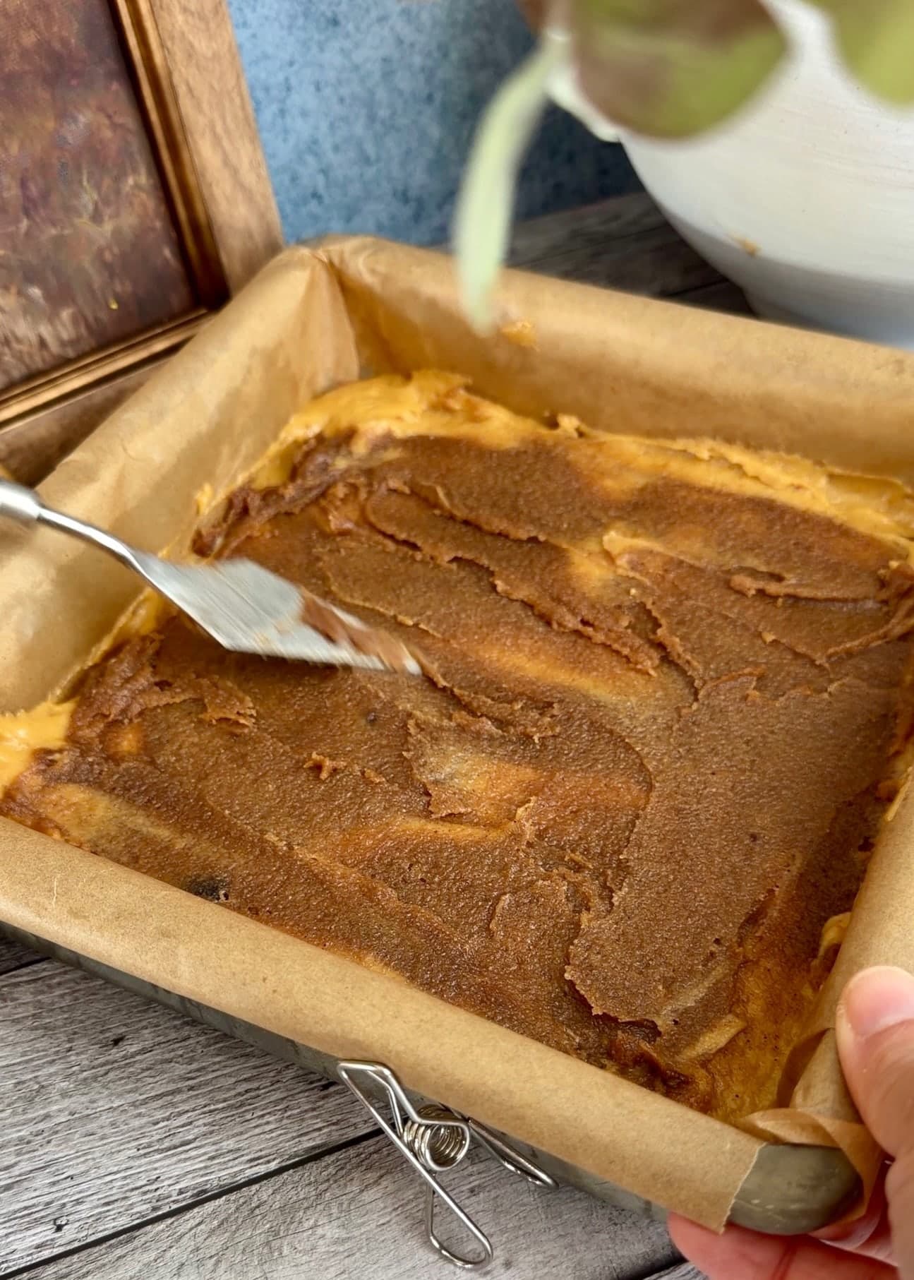 An offset spatula spreading cinnamon paste over the first pumpkin layer