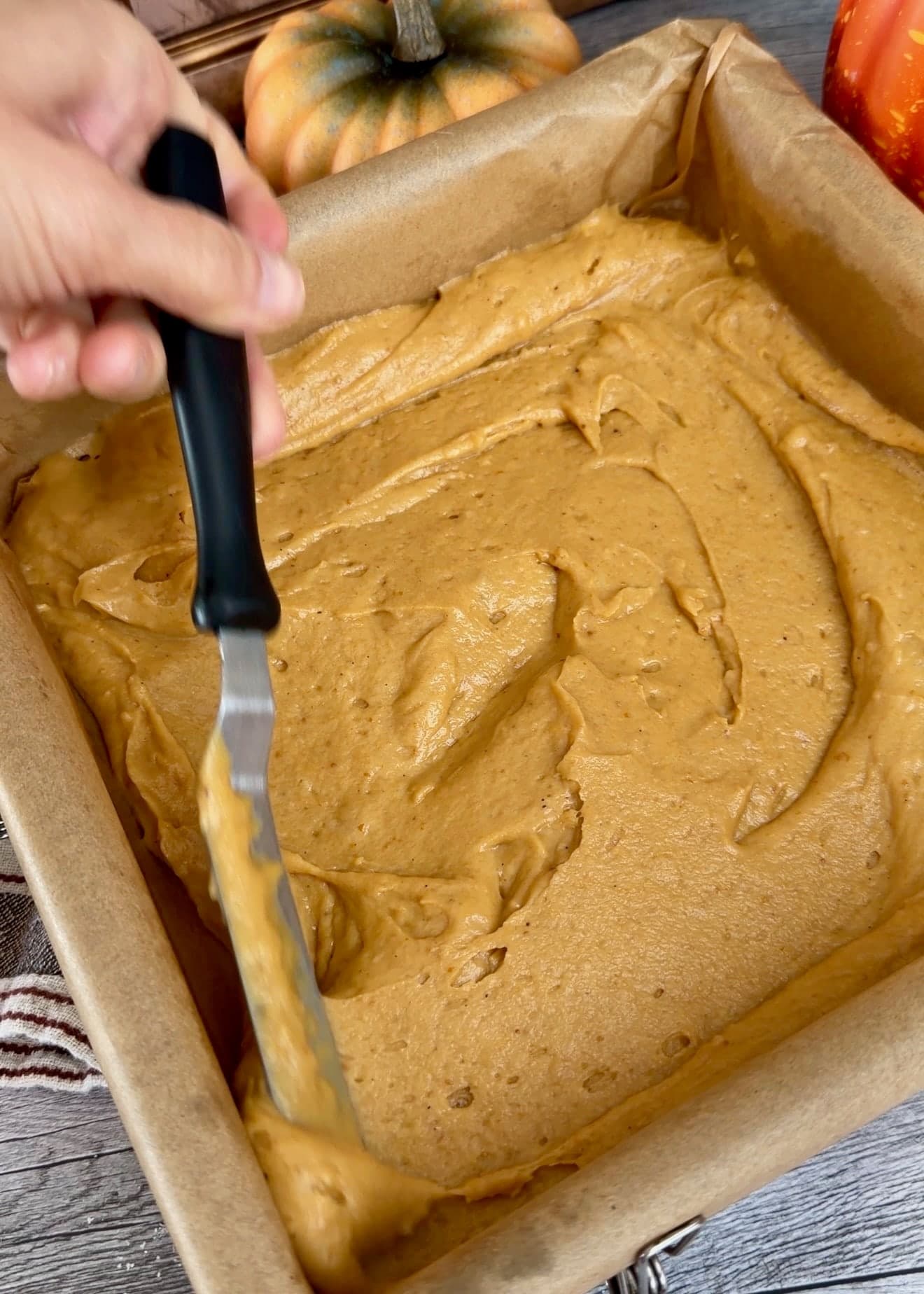 An offset spatula spreading pumpkin batter across the lined pan