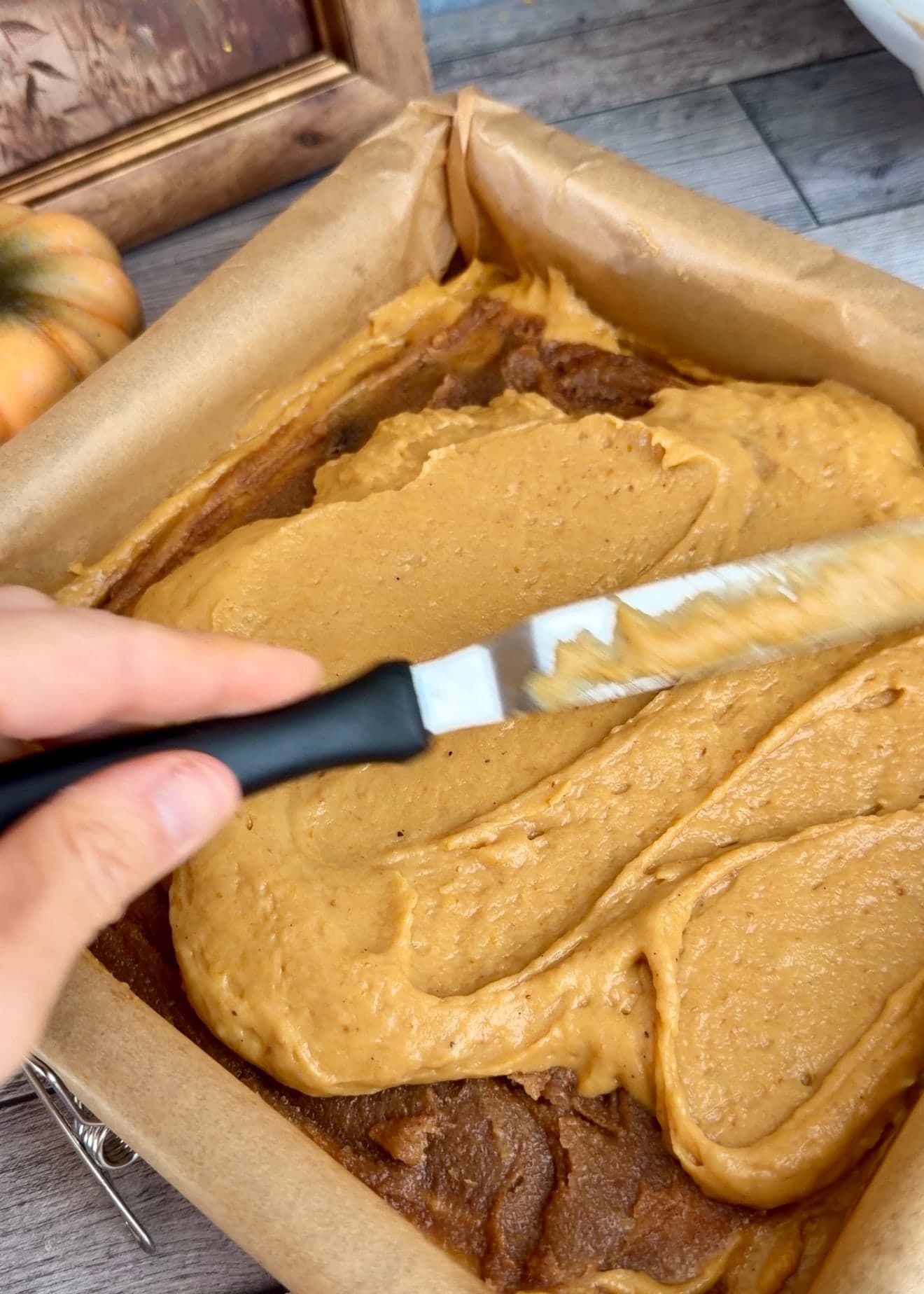 An offset spatula gently spreading the upper pumpkin batter layer