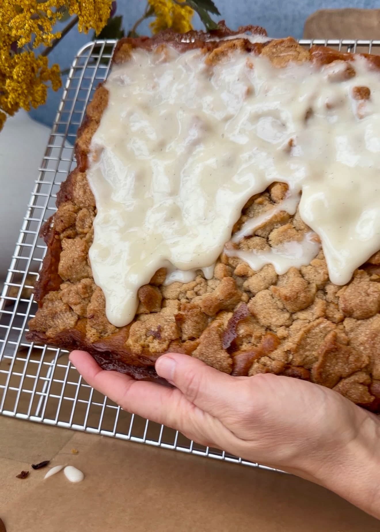 A hand supporting the cake beneath a freshly poured layer of glaze