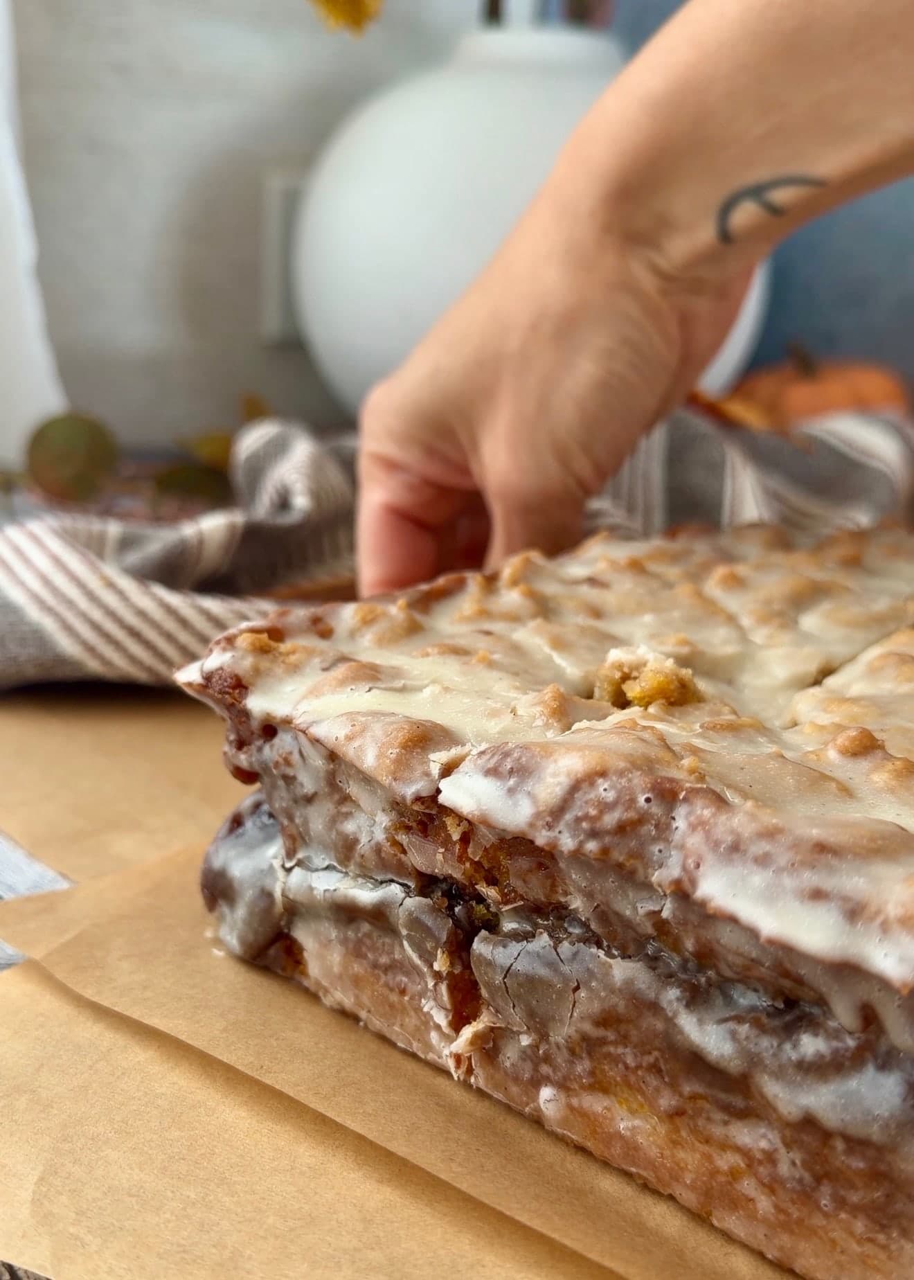 A hand steadying the cake beside a freshly cut glazed edge