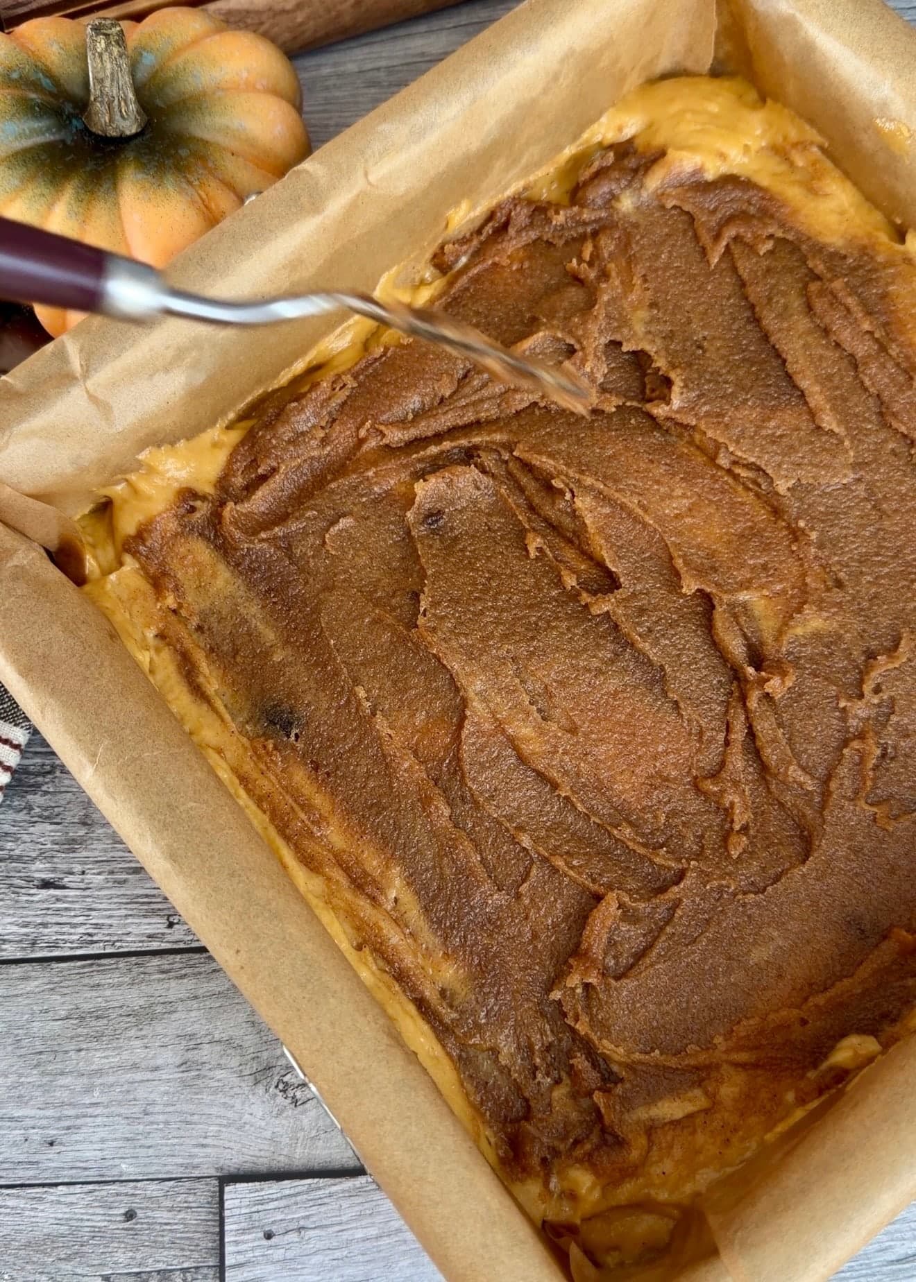 A knife touching the cinnamon layer before making shallow swirls
