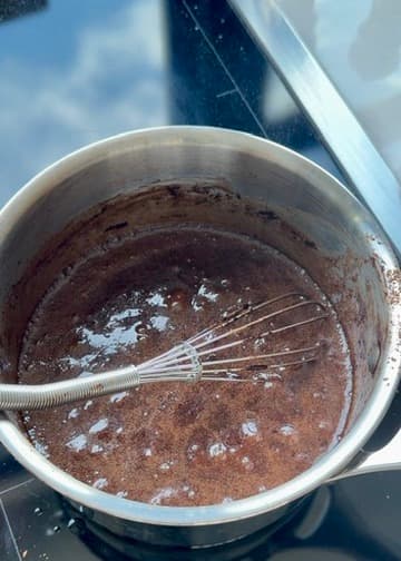 Dark cocoa filling bubbling in a saucepan with a whisk
