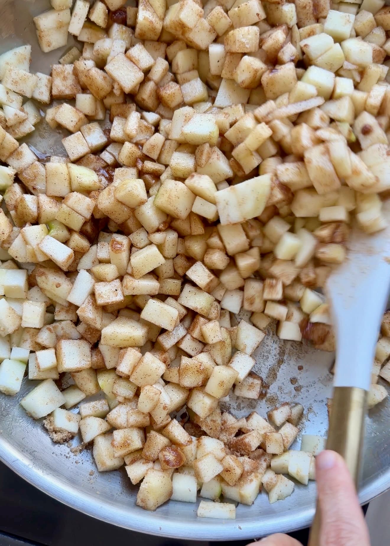 Diced Granny Smith apples cooking with brown sugar and spices in a stainless steel skillet