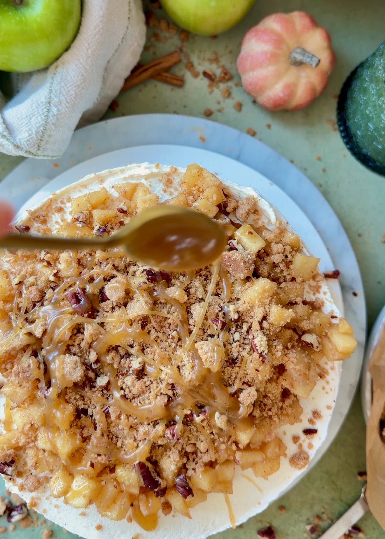 Salted caramel being spooned over apples and pecan streusel on the finished cake
