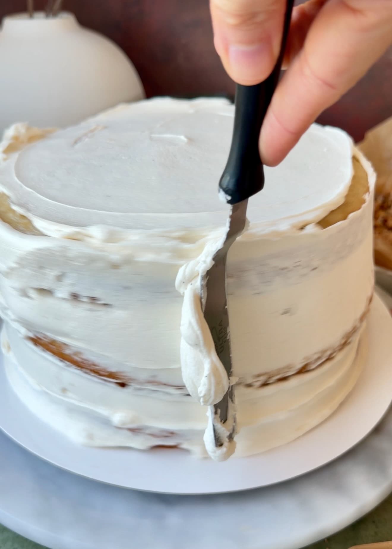 Thin layer of vanilla bean buttercream being spread over the assembled cake
