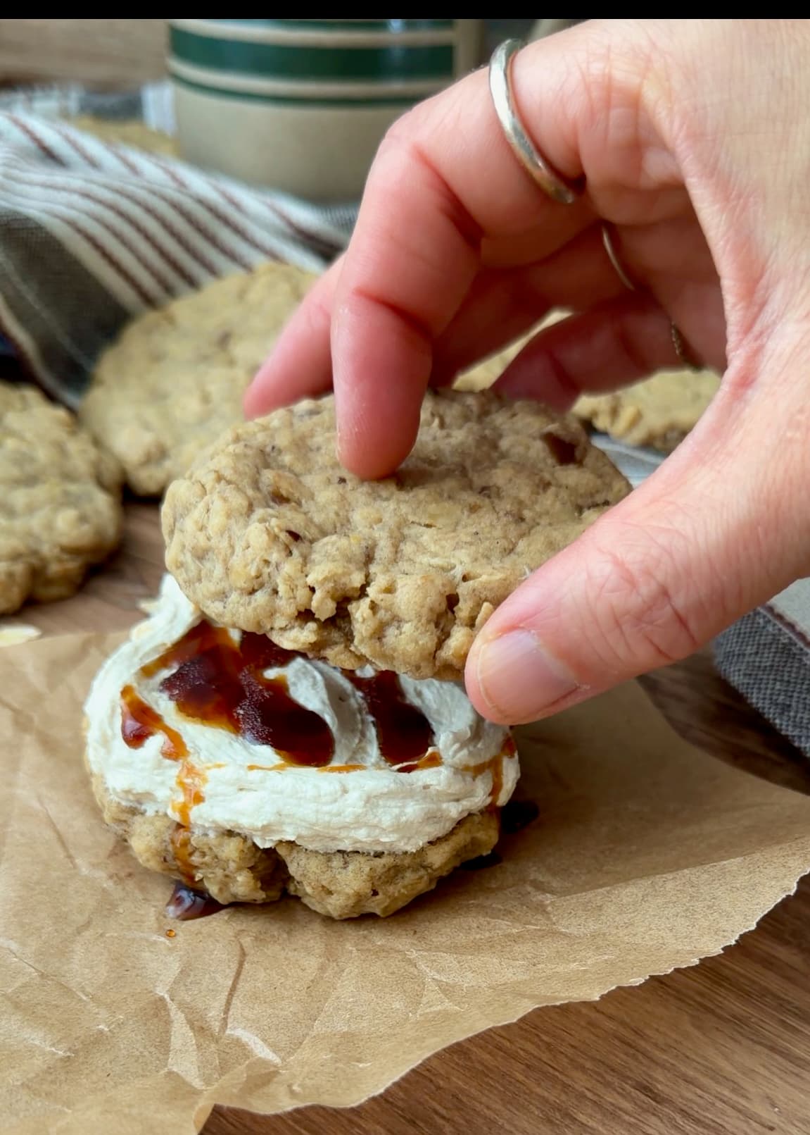 A hand placing a second oatmeal cookie over the cream and caramel filling