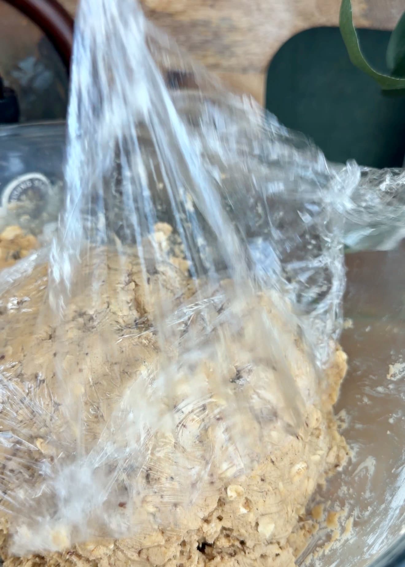 Plastic wrap being placed over a bowl of oatmeal cookie dough