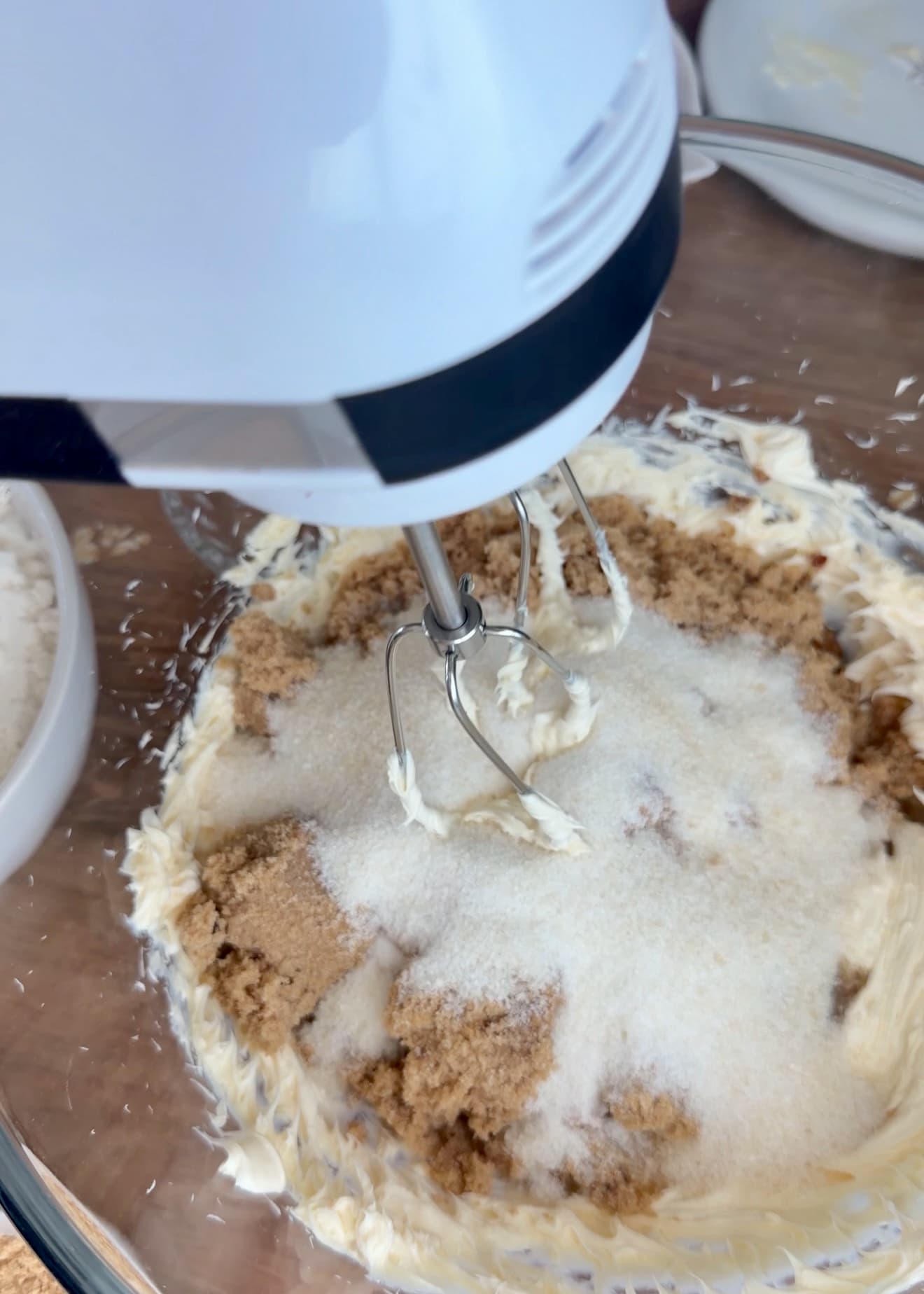 A hand mixer combining butter with brown and granulated sugars in a glass bowl