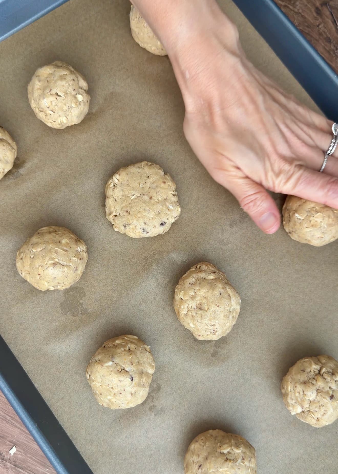 A hand lightly flattening oatmeal cookie dough on a parchment-lined sheet