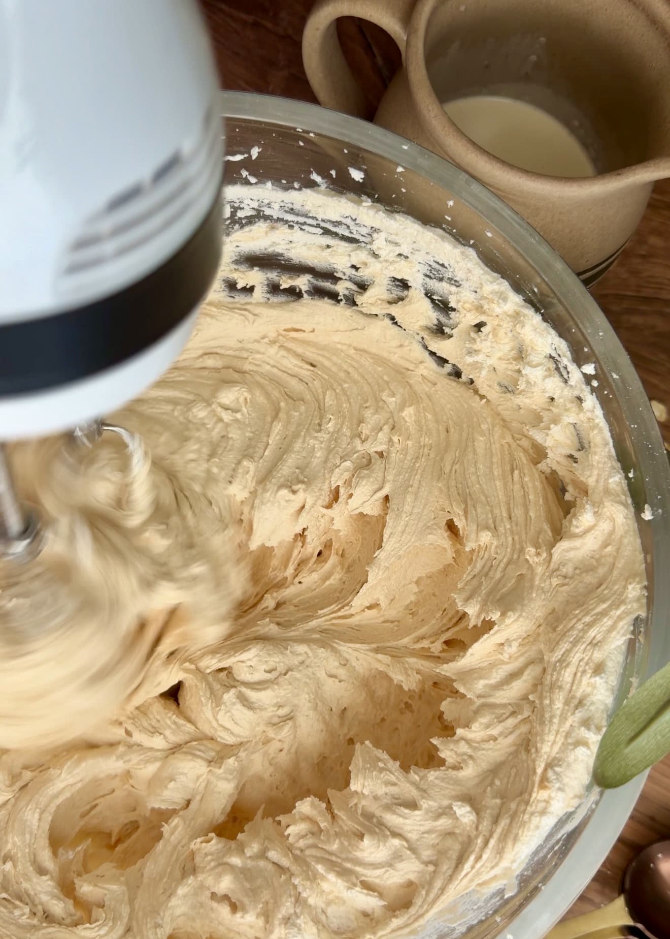 A hand mixer blending the pale caramel cream in a glass bowl
