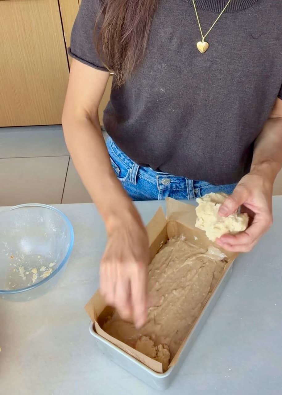 Angela breaking chilled crumble over the first layer of cake batter