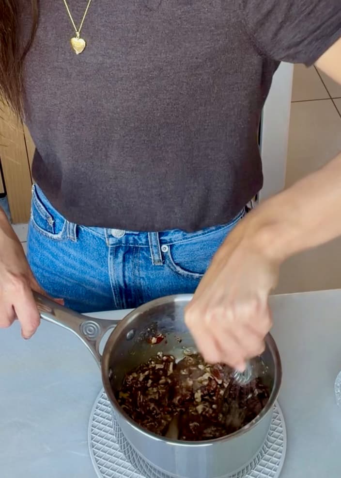 A spoon stirring chopped pecans through the caramel topping