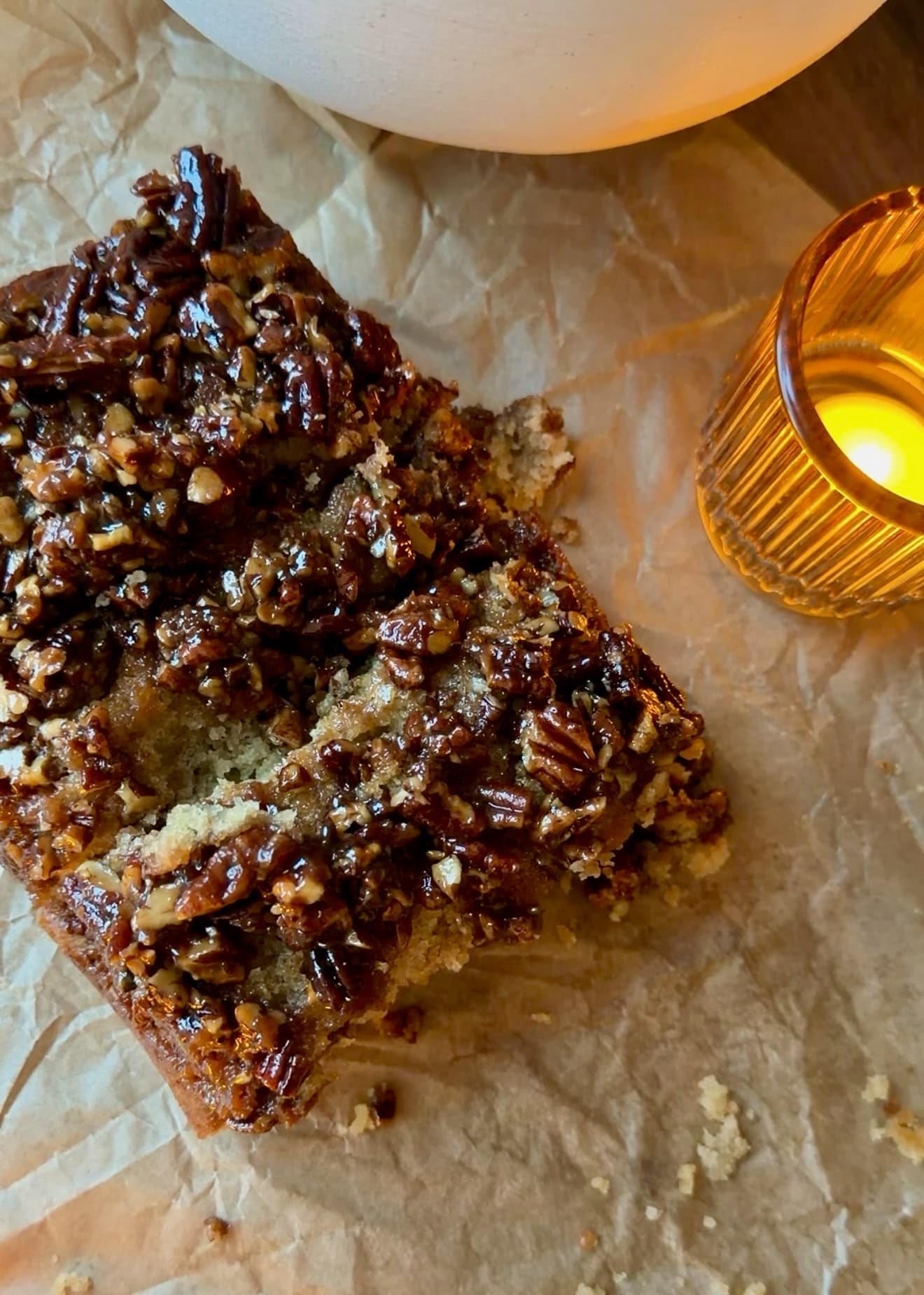 Sticky pecan-topped loaf slices on parchment beside a candle