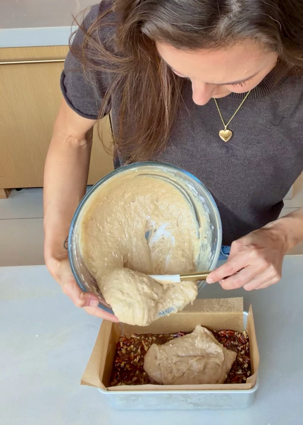 Cake batter being scraped over the pecan topping in the loaf pan