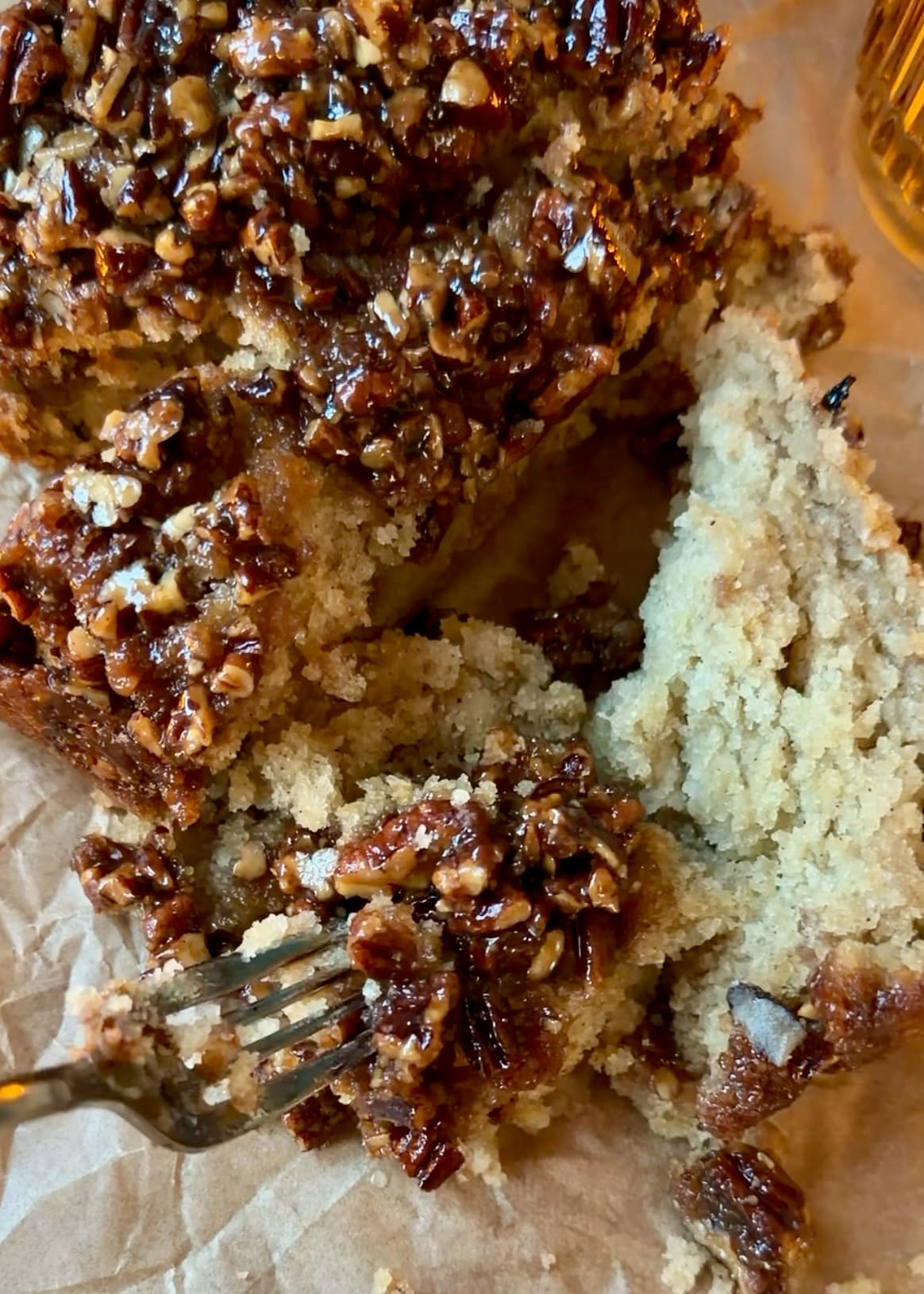 A fork holding a bite of cake and sticky pecans beside sliced loaf