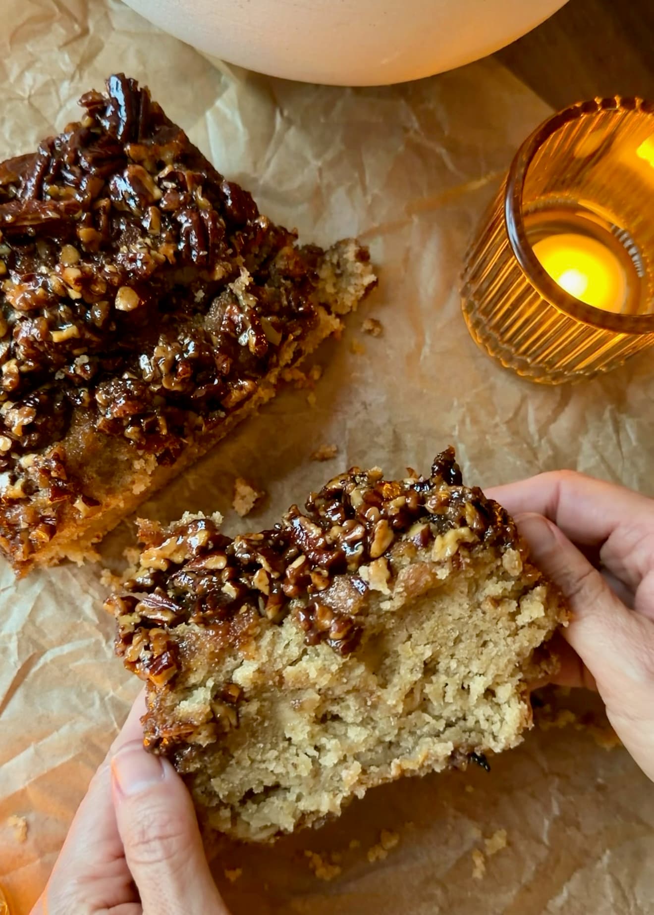 Hands holding a warm slice with caramelized pecans above a soft cake center