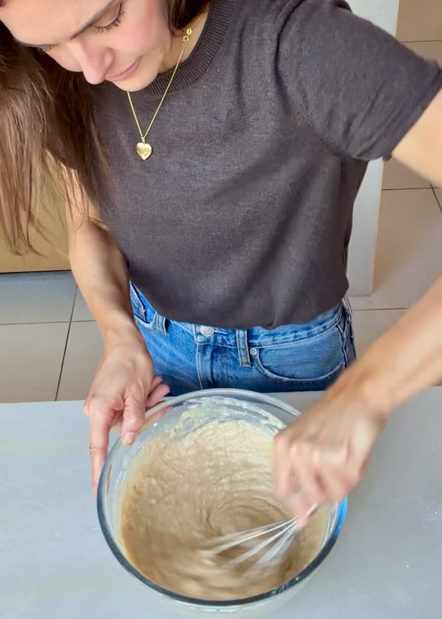 A whisk mixing the cake batter in a glass bowl