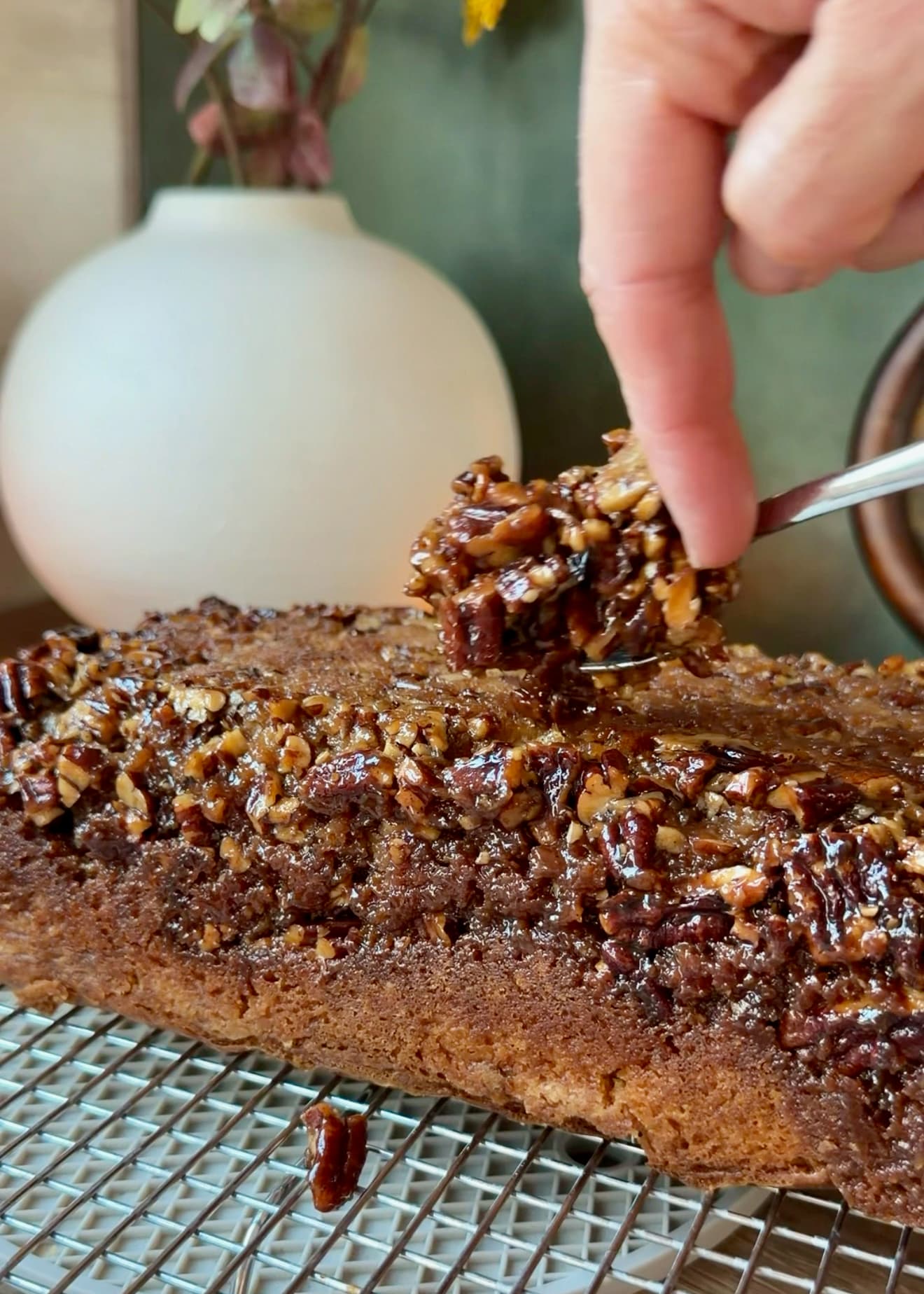A spoon adding caramelized pecans to the edges of the baked loaf